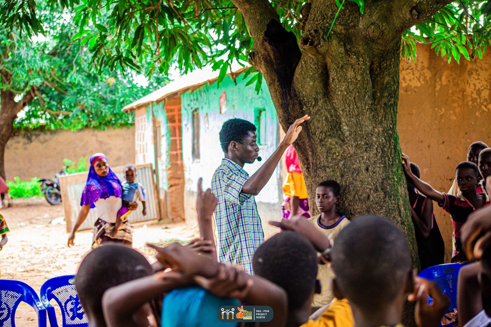 Children gathered under a tree as a team member speaks